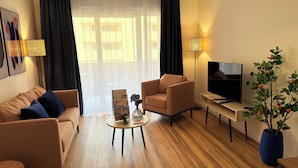 En moderne stue med sofa, lænestol, sofabord, fjernsyn og en potteplante.