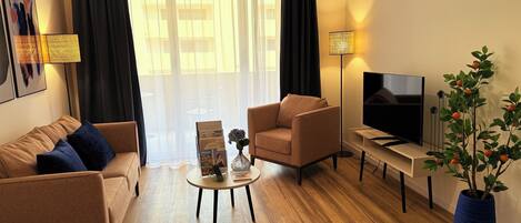 A modern living room with a sofa, armchair, coffee table, TV, and a potted plant.