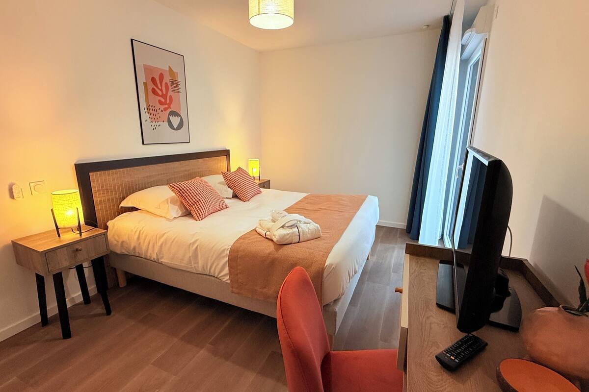 A hotel room with a bed, bedside lamps, a TV, and a window with curtains.