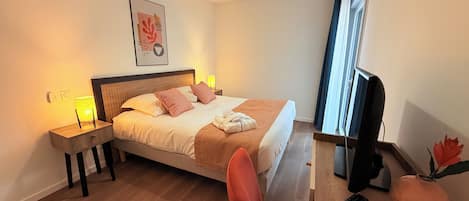 A hotel room with a bed, bedside lamps, a TV, and a window with curtains.