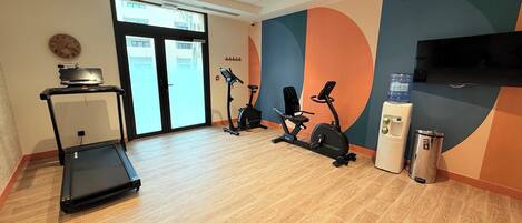 Un gimnasio con cinta de correr, bicicletas estáticas y un dispensador de agua.