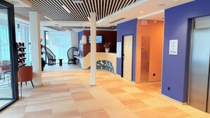 En moderne hotellobby med reception, siddeområde og trappe til en etage ovenover.