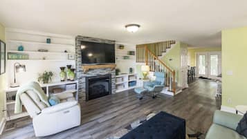 Ein Wohnzimmer mit Kamin, Fernseher und einer Treppe, die in einen anderen Raum führt.