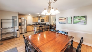 A spacious kitchen with modern appliances, a dining area with a large wooden table, and three framed pictures on the wall. - Four Bedroom 4.5 Bath Condo (Grand Rivers)