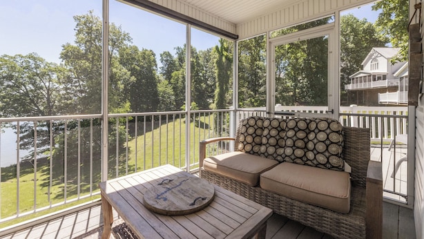 A covered porch with a wicker sofa and a wooden table, overlooking a lake and a house. - Four Bedroom 4.5 Bath Condo (Grand Rivers)