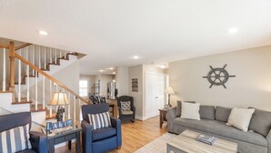 A living room with a staircase, a grey sofa, a blue armchair, and a ship's wheel decoration on the wall. - Four Bedroom 4.5 Bath Condo (Grand Rivers)