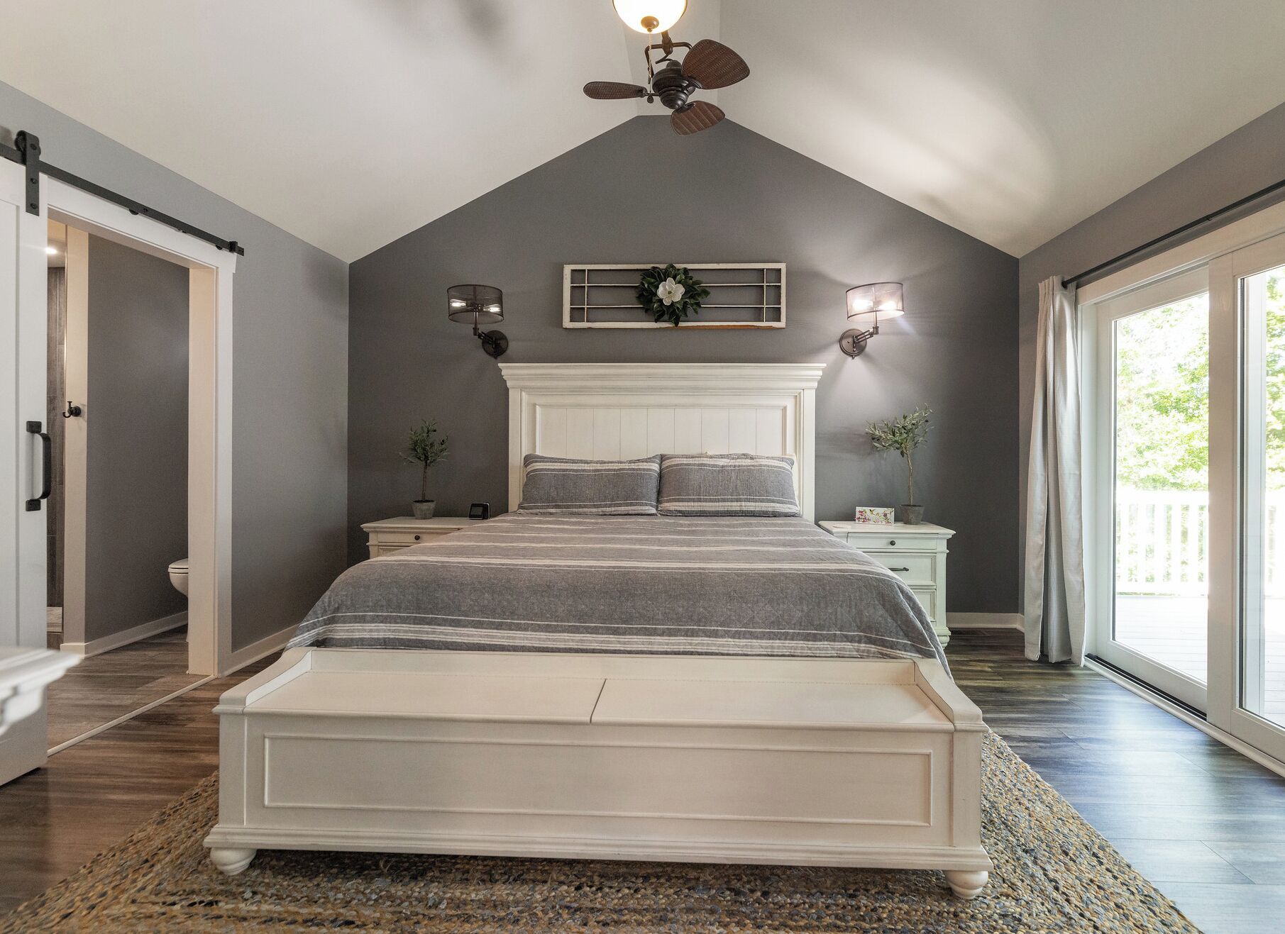 Quarto com uma cama grande, ventilador de teto, janela com cortinas e vista para o exterior.