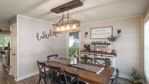 A dining area with a wooden table and chairs, a decorative wall with the word "Lakelove," and a kitchen area with a coffee machine and plants. - Four Bedroom Yacht Condo (Grand Rivers)