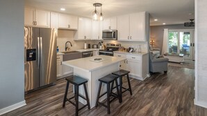 A modern kitchen with white cabinetry, stainless steel appliances, and a central island with stools. - Four Bedroom Yacht Condo (Grand Rivers)