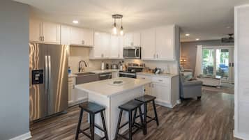 A modern kitchen with white cabinetry, stainless steel appliances, and a central island with stools.
