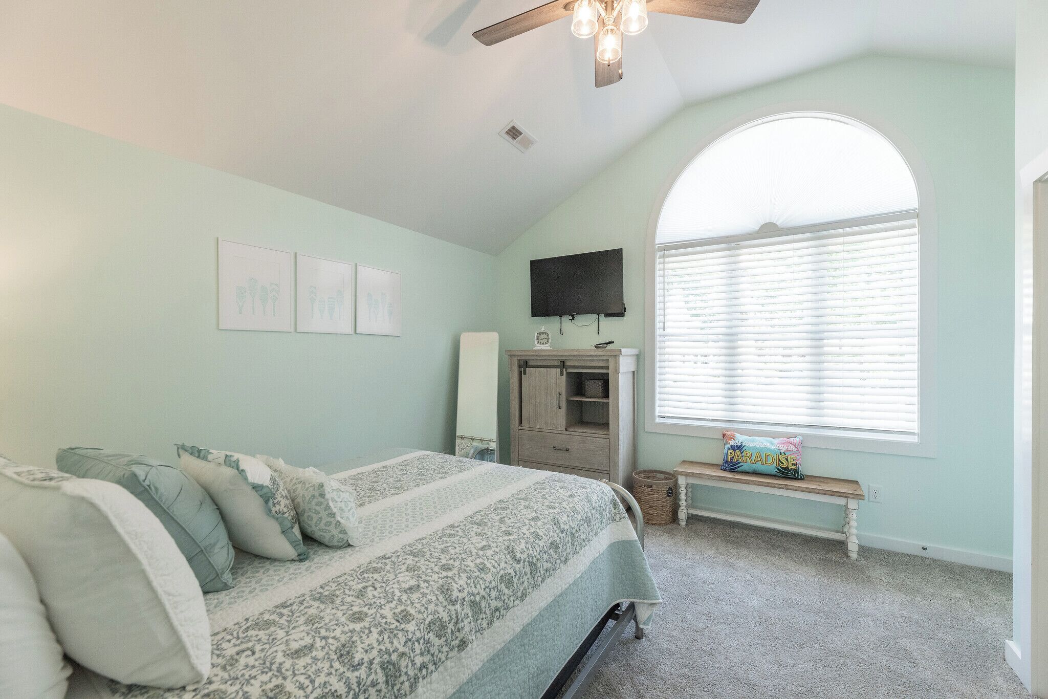 A bedroom with a bed, a bench, a TV, and a window with blinds.
