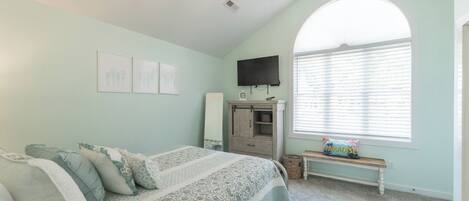 A bedroom with a bed, a bench, a TV, and a window with blinds.