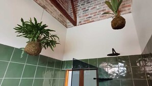 Ein Badezimmer mit grünen Fliesen, einer Dusche und zwei hängenden Pflanzen.