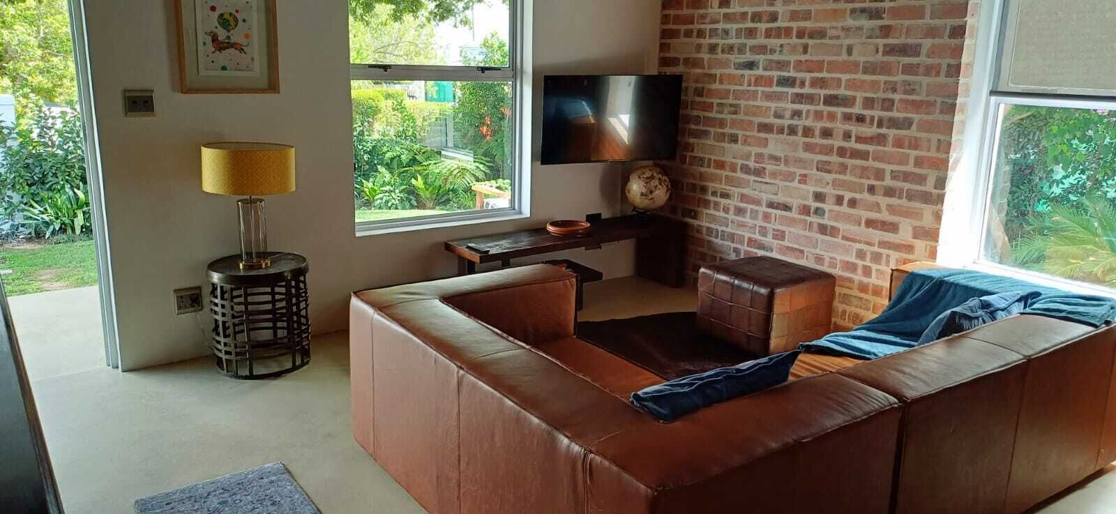 A living room with a leather sofa, a TV, and a brick wall.