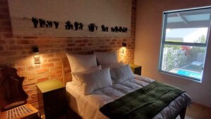 Ein Schlafzimmer mit Backsteinwand, einem Bett mit weißer Bettwäsche, zwei Nachttischen und einem Fenster mit Blick nach draußen.