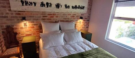 A bed with white linens, a brick wall, and a window with a view.