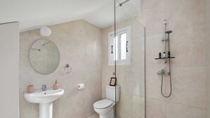 Un baño moderno con cabina de ducha de vidrio, espejo redondo, lavabo sobrepedal y retrete.