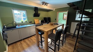 Une cuisine compacte avec une table et des chaises en bois, un poêle noir et une fenêtre donnant sur un paysage verdoyant.