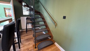 Un escalier avec des marches en bois et des rampes en métal, menant à un palier où se trouvent une table à manger et des chaises.