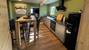 Une cuisine moderne avec un coin repas, un plancher en bois, un réfrigérateur noir et une fenêtre agrémentée de plantes.