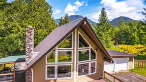 A small, single-story cabin with multiple windows and a stone chimney, surrounded by lush greenery and mountains. - Cottonwood Chalet in Packwood (Packwood)