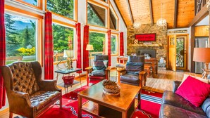 A spacious living room with large windows, a stone fireplace, and a cozy seating area with leather sofas and armchairs. - Cottonwood Chalet in Packwood (Packwood)