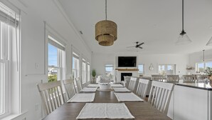 Un comedor con una mesa de madera, sillas blancas y una lámpara colgante de fibras naturales.