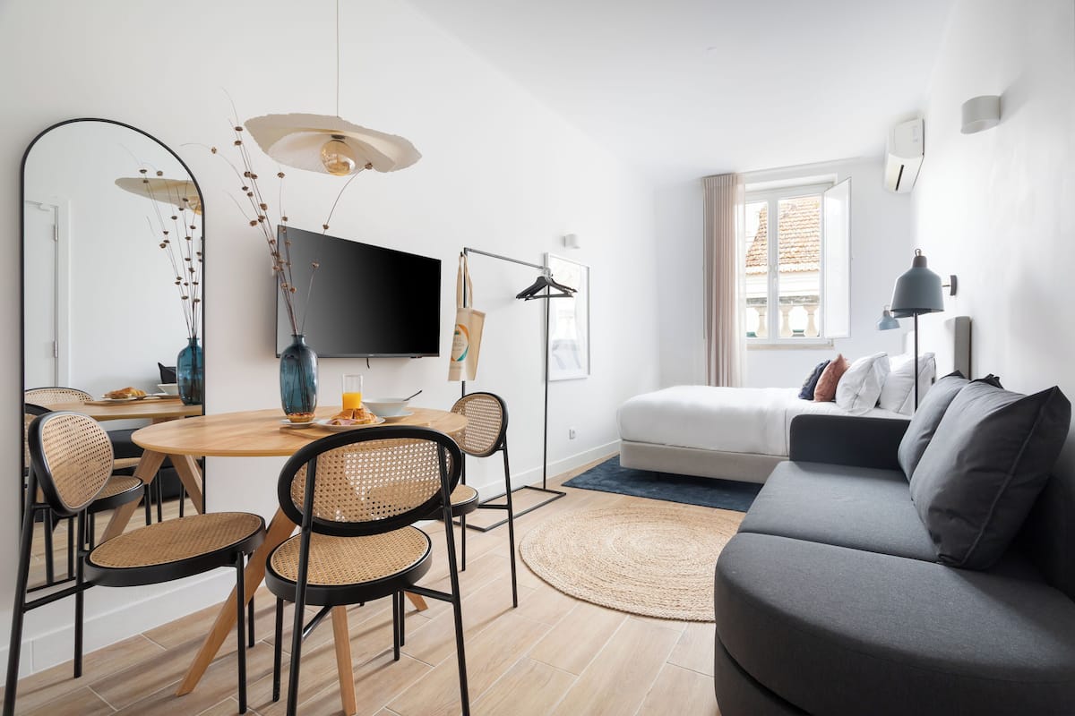 Una sala de estar moderna con un sofá gris, una mesa de comedor con sillas, un televisor de pantalla plana y un espejo grande.