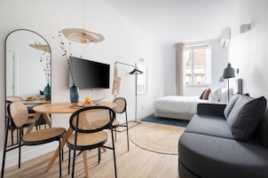 Una sala de estar moderna con un sofá gris, una mesa de comedor con sillas, un televisor de pantalla plana y un espejo grande.