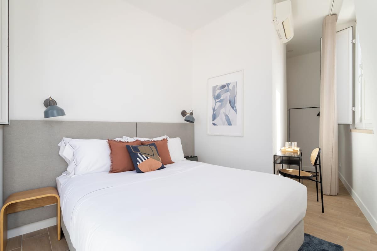 Un dormitorio moderno con una cama grande, una mesita de noche, una silla y un escritorio pequeño con silla.