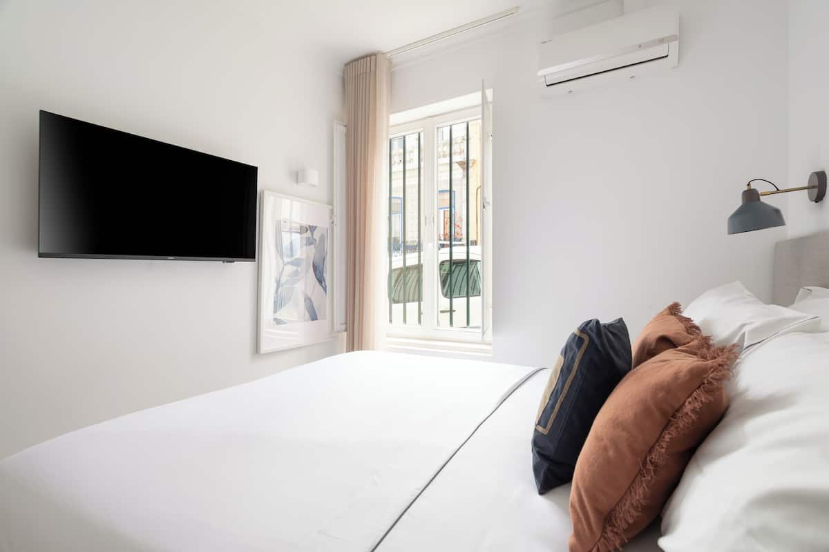 Una habitación de hotel moderna con un televisor de pantalla plana en la pared, una cama grande con ropa blanca y un ventanal con vistas al exterior.