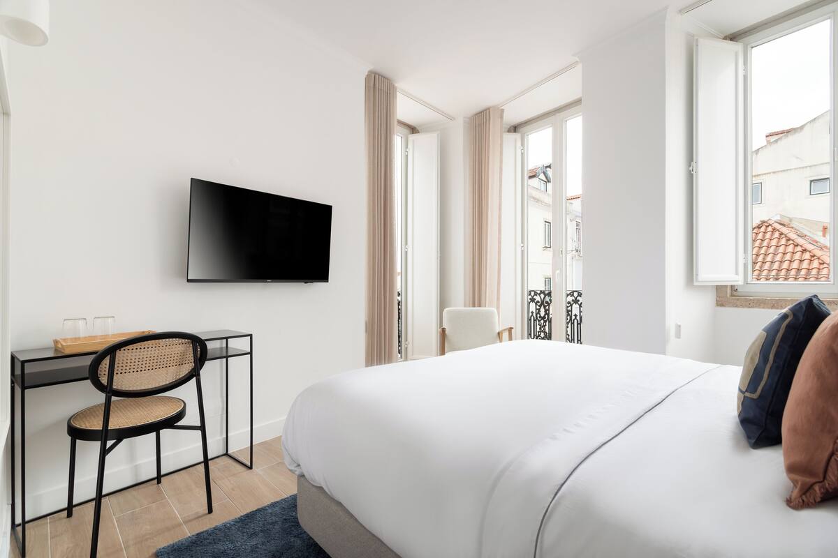 Habitación de hotel con cama, escritorio con silla, televisor y ventana con cortinas.