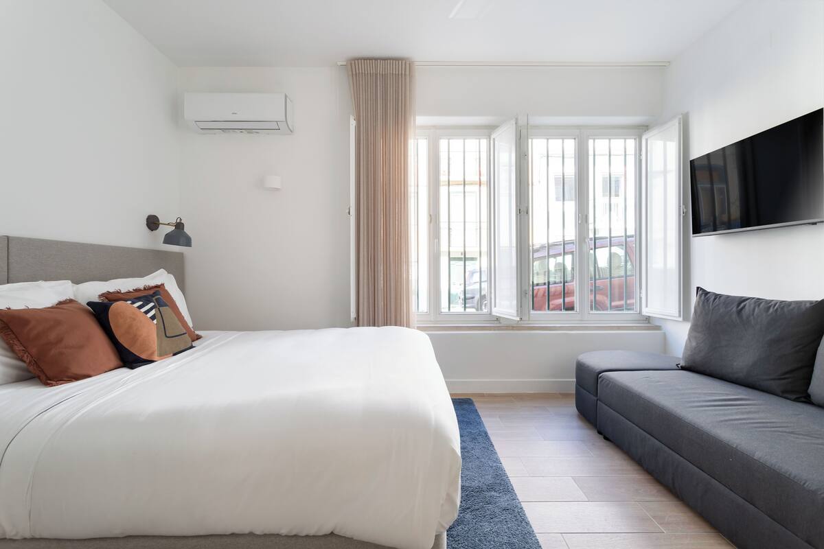 Un dormitorio con cama, sofá, televisión y ventana con cortinas.