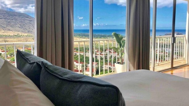 Une chambre d’hôtel dotée d’une grande fenêtre donnant sur la mer et sur une chaîne de montagnes lointaine.