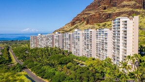 Un grand hôtel à plusieurs étages, une route au premier plan et un paysage montagneux en arrière-plan.