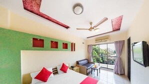 A hotel room with a large bed, a ceiling fan, a balcony with a view, and a TV on the wall. - Neeta's Sagar Inn (Lonavala)