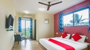 A hotel room with a bed, a desk, a chair, a television, and a window with curtains. - Neeta's Sagar Inn (Lonavala)