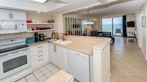 A modern kitchen with white appliances, a large island, and a view of the sea through the balcony.