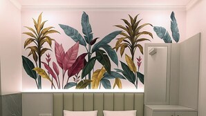 Une chambre à coucher comprenant un lit, une table de chevet, un miroir et un mur orné d’une fresque représentant des feuilles tropicales.