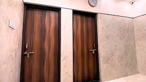Une pièce dotée de deux portes en bois, d’un sol en marbre, d’un luminaire au plafond et d’une horloge murale.