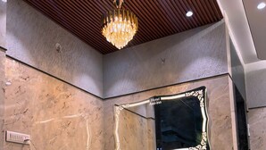 Un intérieur moderne avec un mur en marbre, un banc jaune, un lustre et un miroir encadré.