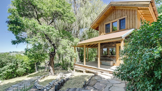 A wooden cabin with a porch, surrounded by trees and a stone pathway. - Historic Nature Lovers Cabin on Farm in Paonia! (Paonia)