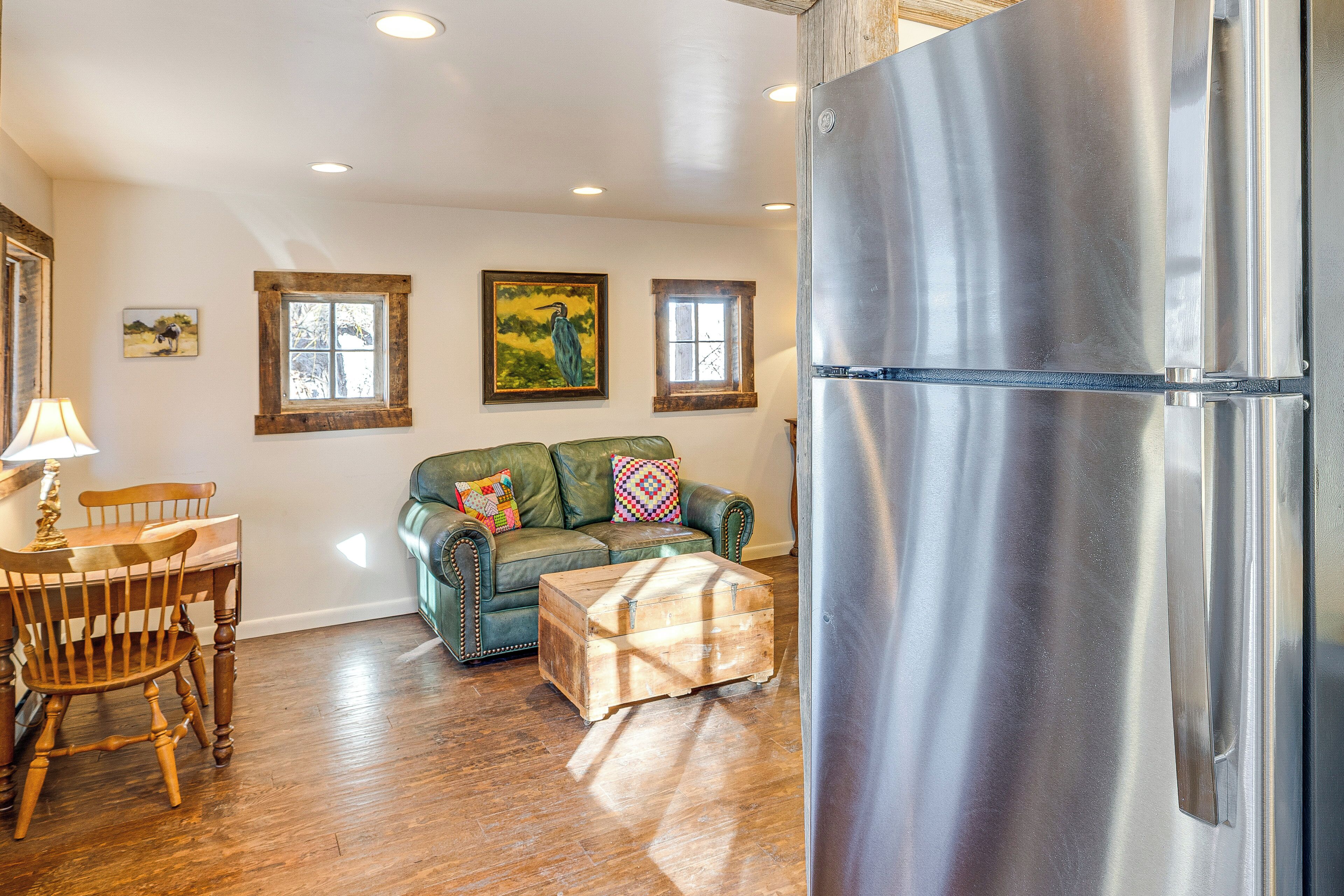 A living room with a wooden dining table, a green sofa, a wooden chest, and a stainless steel refrigerator.