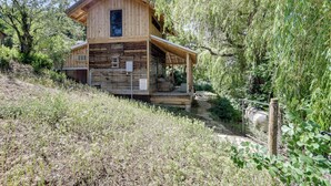 A wooden cabin with a porch, surrounded by trees and a grassy area. - Historic Nature Lovers Cabin on Farm in Paonia! (Paonia)