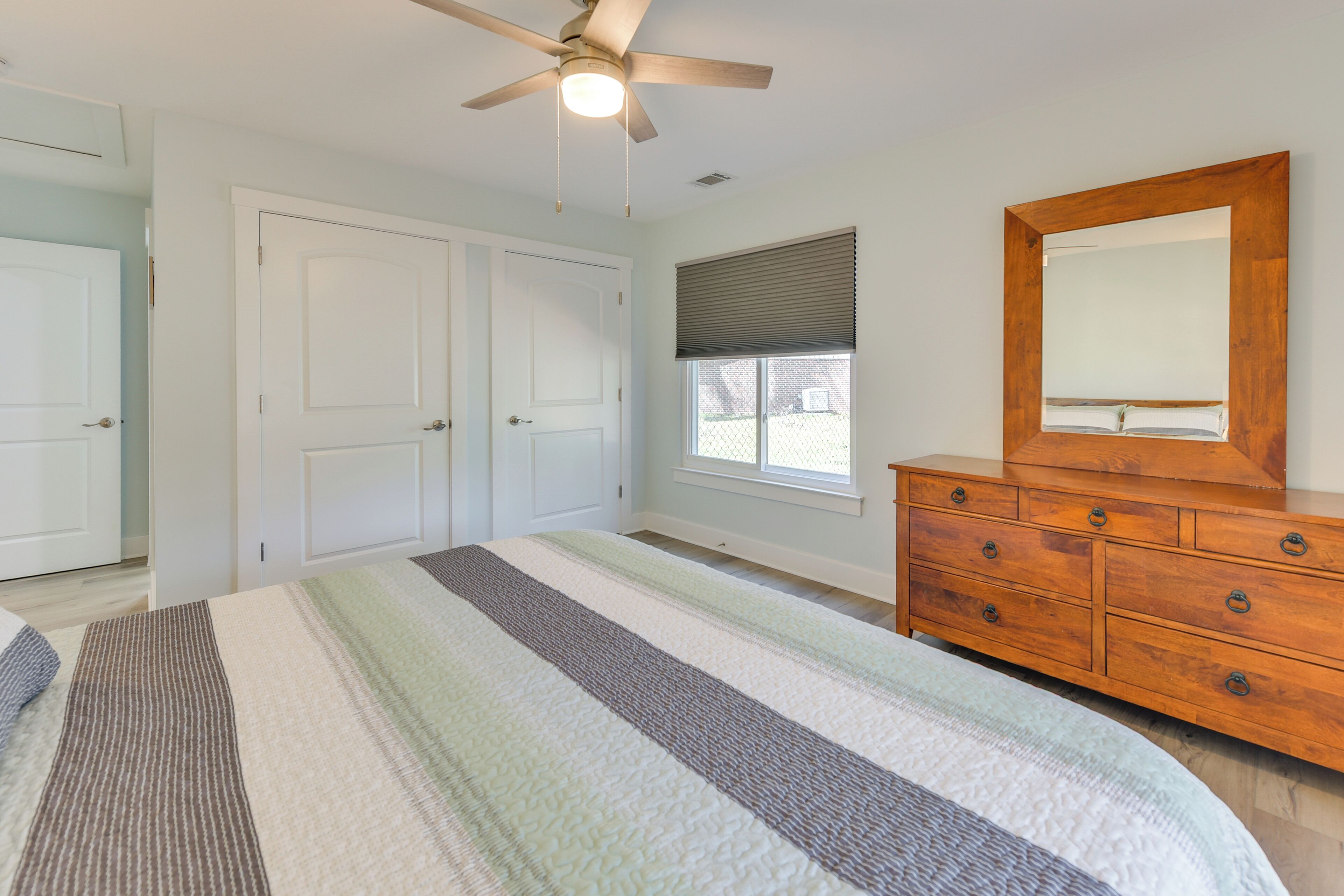 Une chambre à coucher avec un lit, une commode en bois, un ventilateur de plafond et une fenêtre avec des stores.