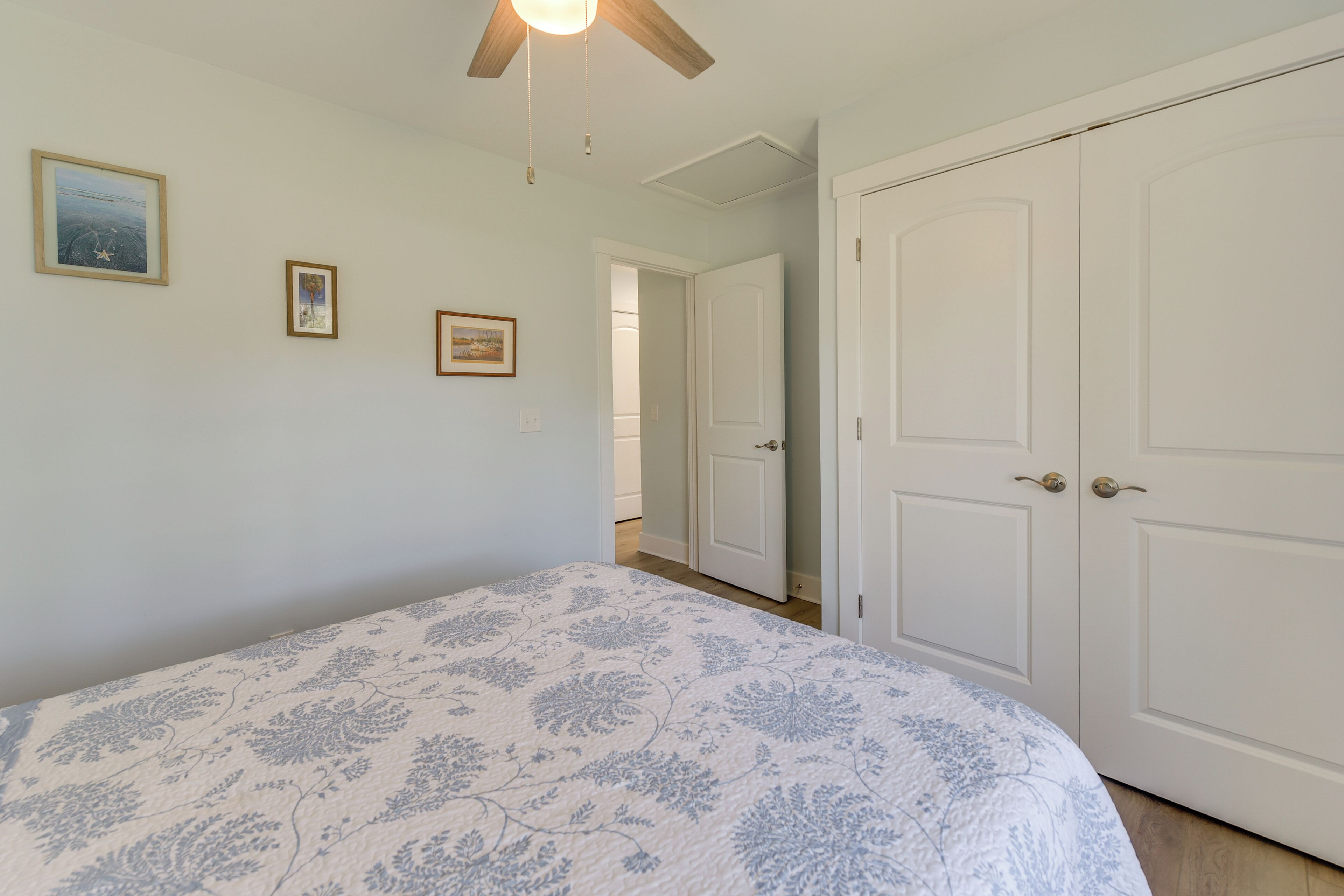 A bedroom with a bed, a ceiling fan, and a door leading to another room.
