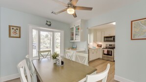 A dining area with a wooden table and white chairs, a ceiling fan, and a view of the kitchen with white cabinets and appliances. - 5 Mi to Dtwn Beaufort: Home w/ Screened-in Patio (Port Royal)