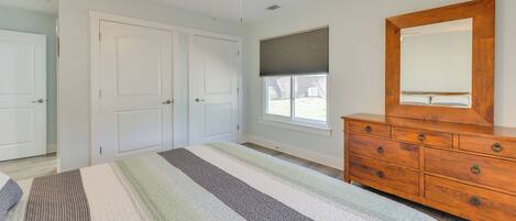 A bedroom with a bed, a wooden dresser, a ceiling fan, and a window with blinds.