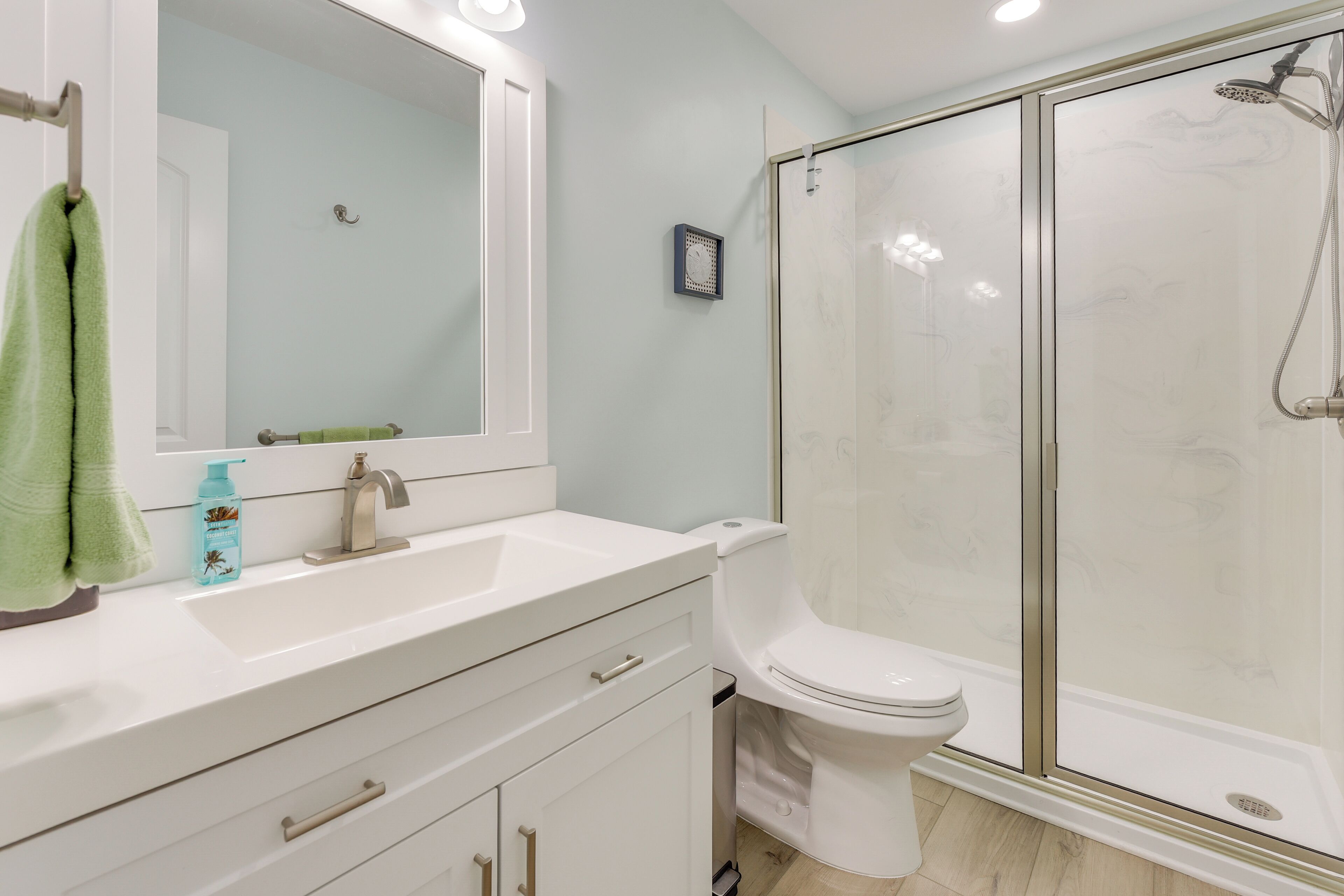 A bathroom with a white sink, a mirror, a toilet, and a glass shower enclosure.