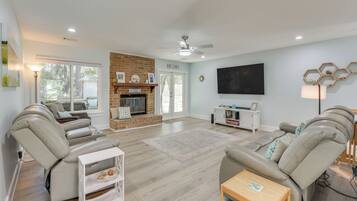 A spacious living room with a fireplace, leather sofas, a flat-screen TV, and a ceiling fan.